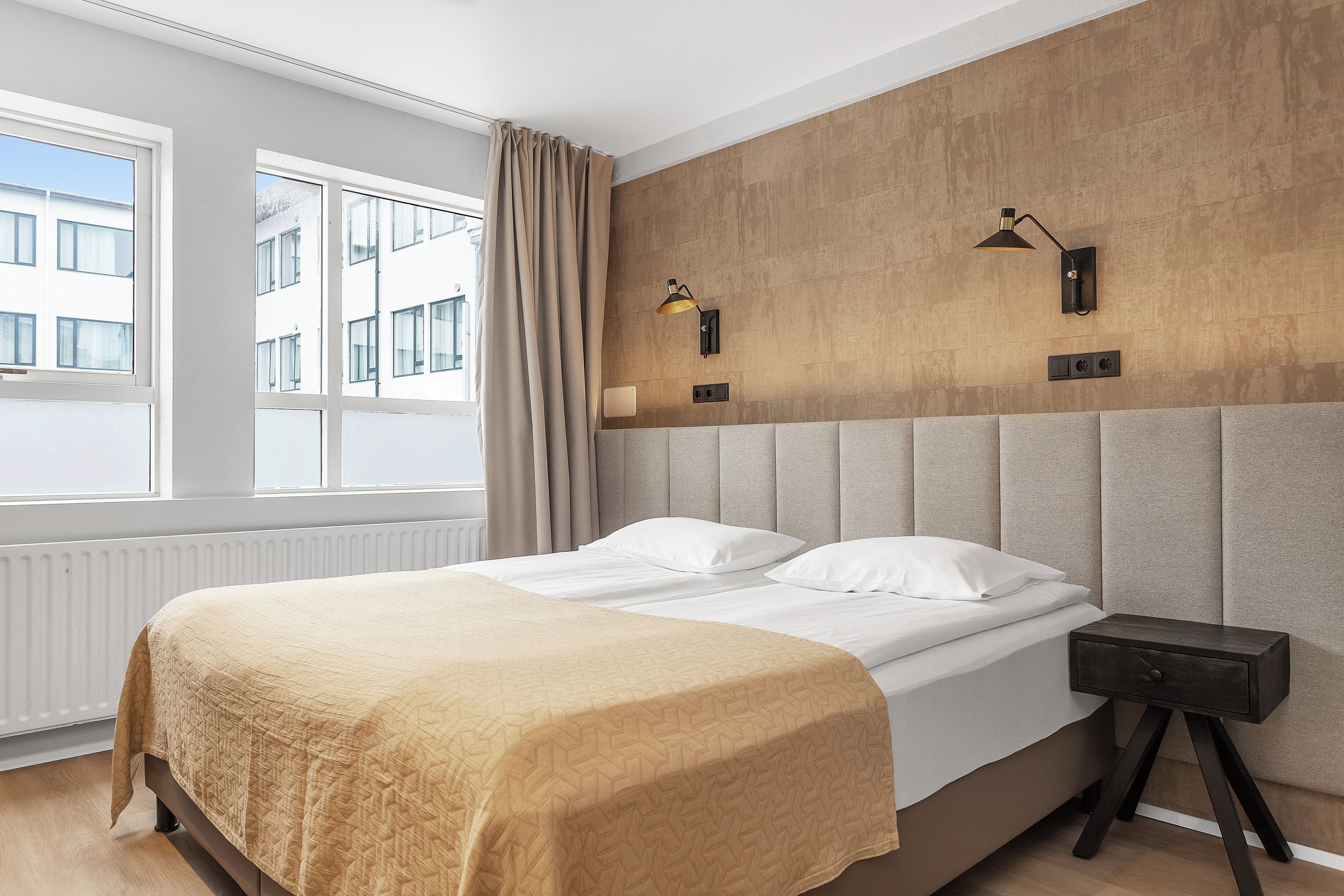 Een slaapkamer met een groot bed, twee nachtkastjes, een hoofdeinde en een raam met gordijnen.
