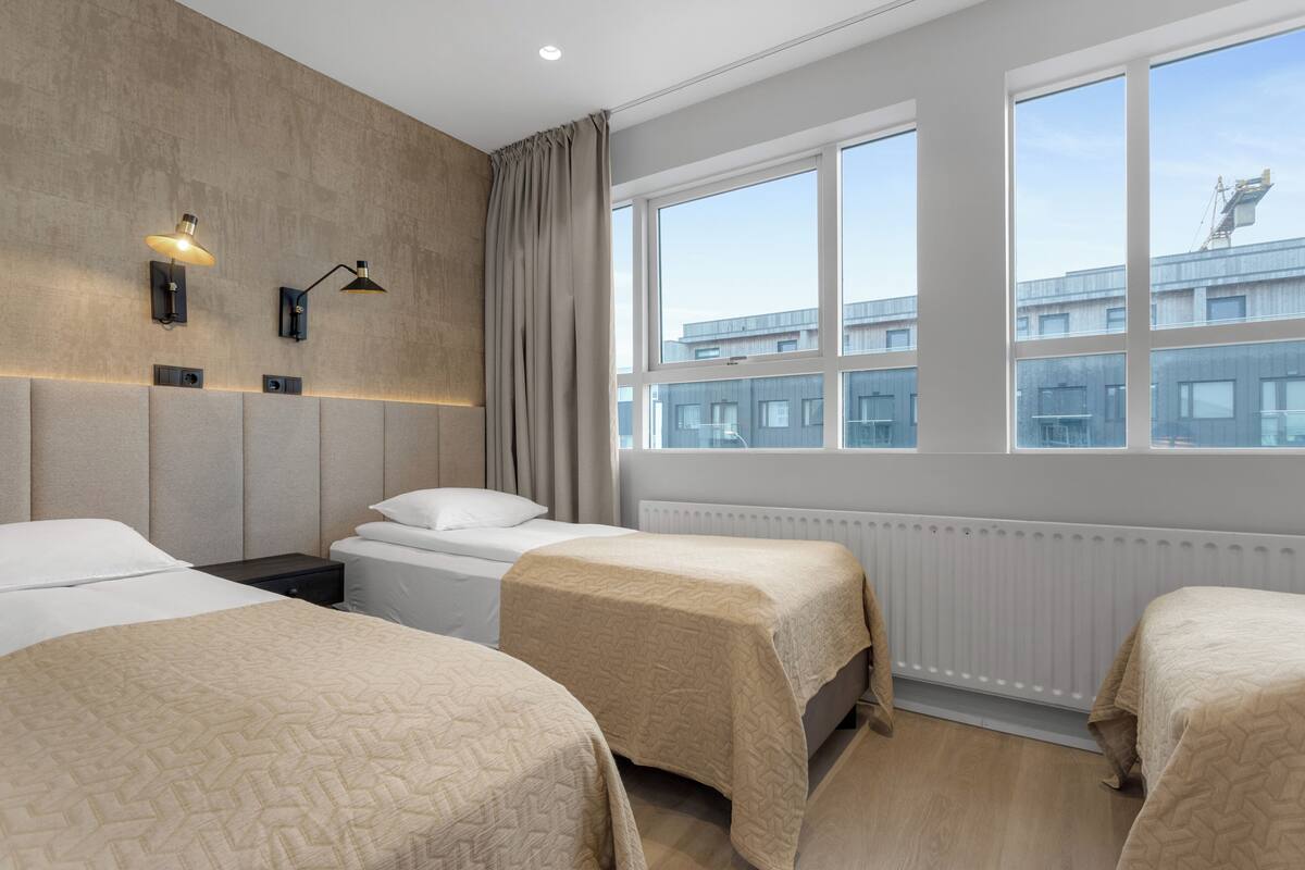 Hotellihuone, jossa on kaksi sänkyä, suuri ikkuna, patteri ja näkymä ulkona oleviin rakennuksiin.