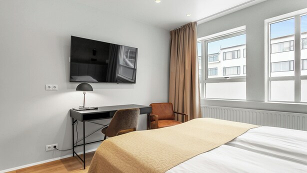 Una habitación de hotel con cama, escritorio con silla, televisor y ventana con cortinas.