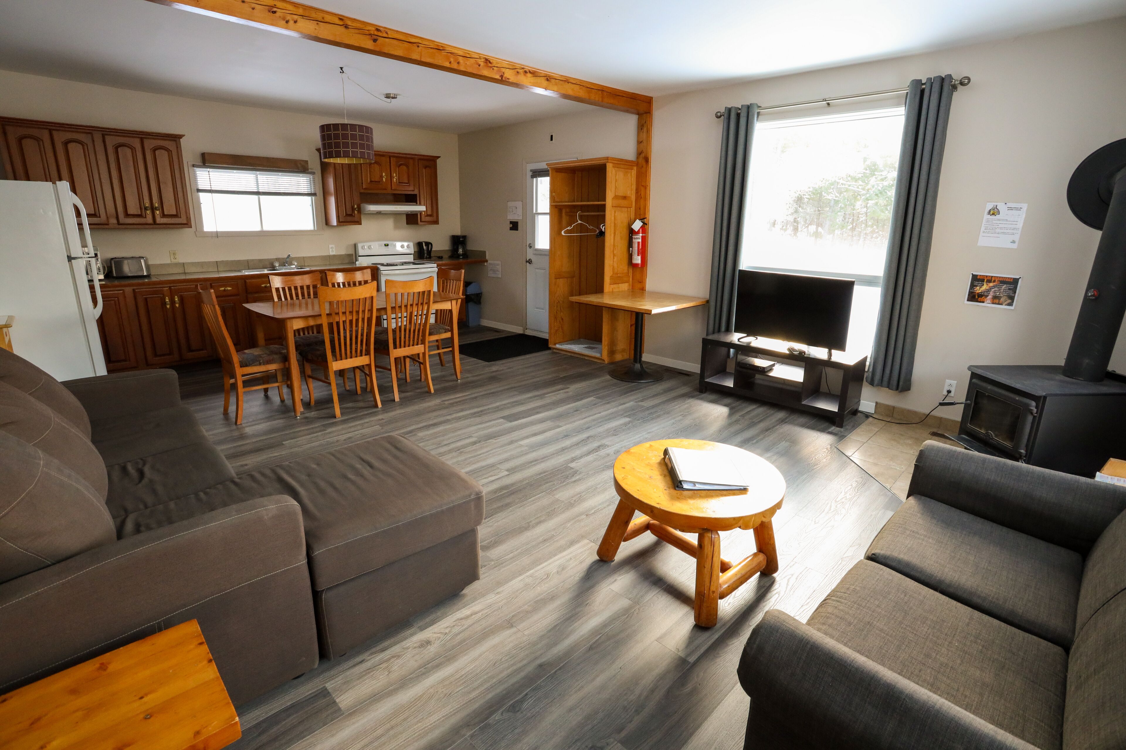 A modern living room with a sofa, a coffee table, and a TV. There is a kitchen area with wooden cabinets and a dining table.