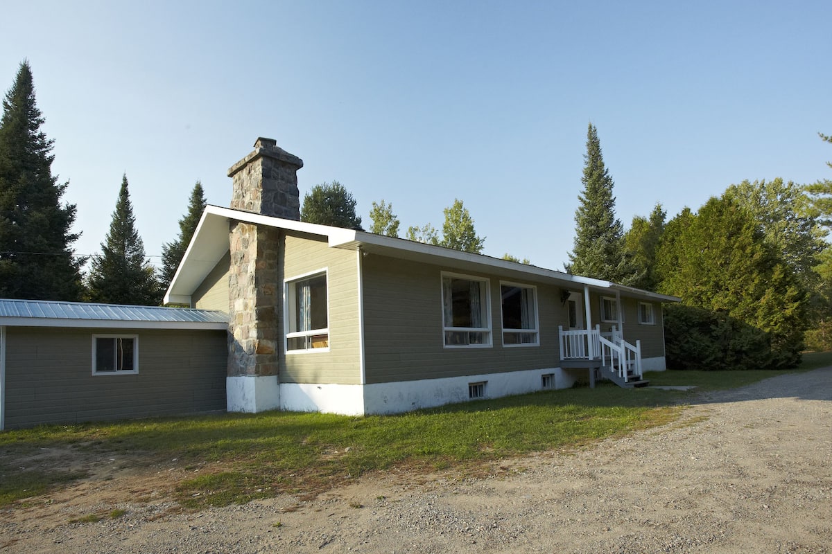 A two-story house with a stone chimney, a front porch, and a gravel driveway.