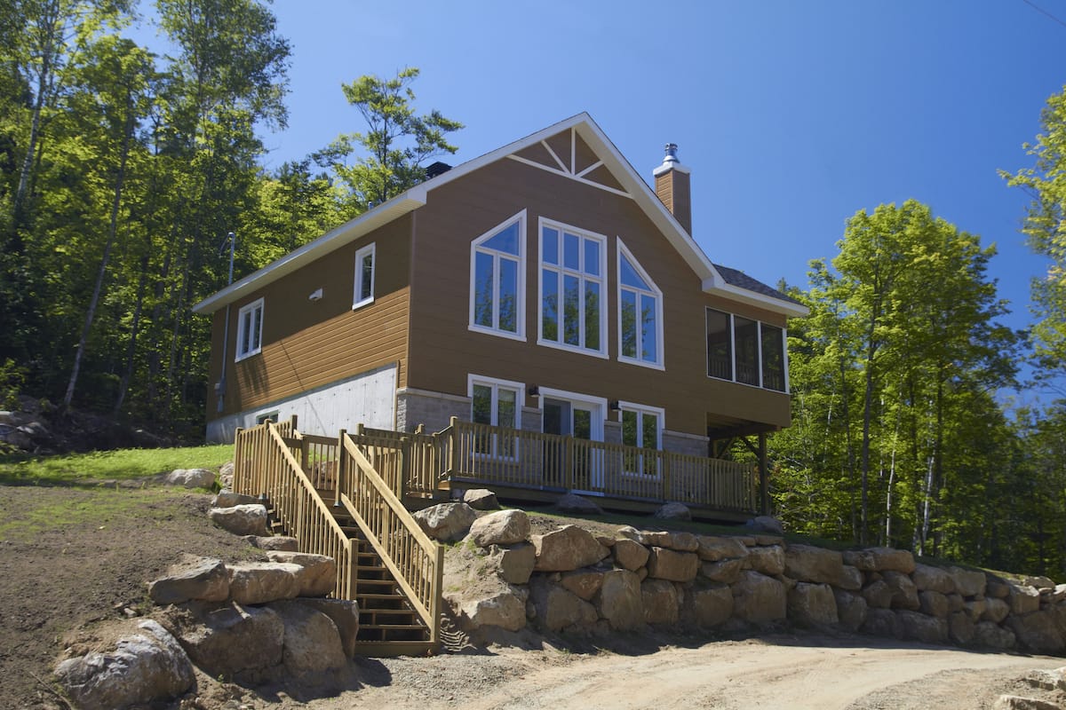 A two-story house with a stone foundation, wooden deck, and a staircase leading to the entrance.