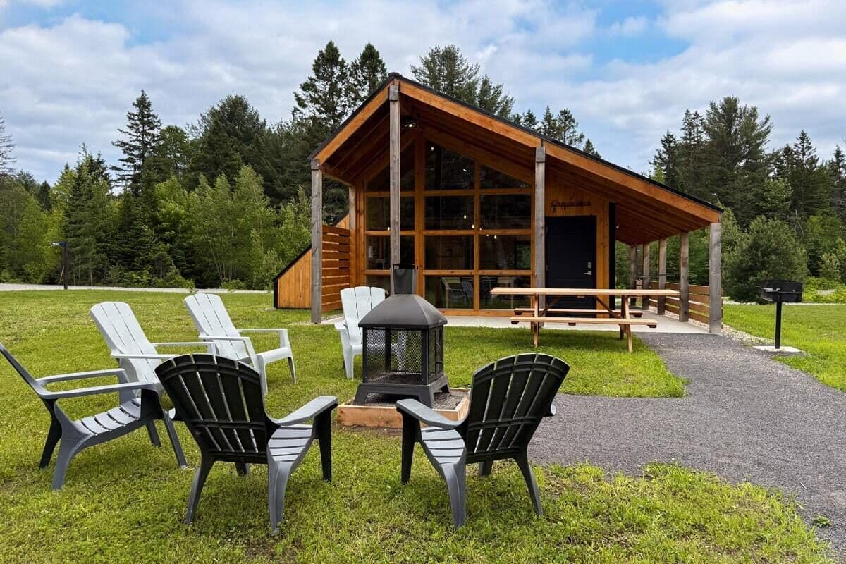 A lodge with a wooden exterior, large windows, and a fire pit area with chairs.