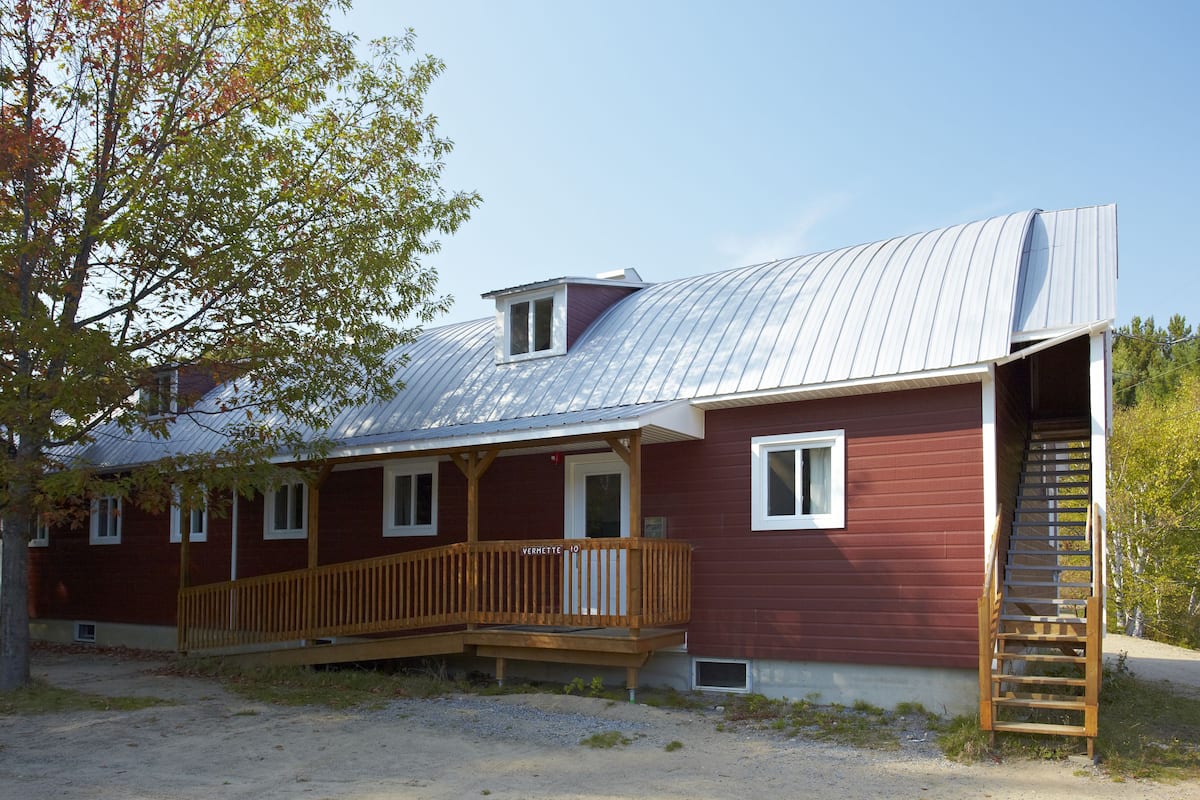 A red building with a metal roof, a wooden deck, and a staircase leading to a second floor.
