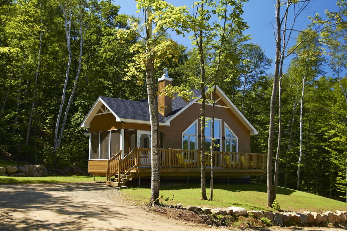 A cabin with a porch, large windows, and a chimney.