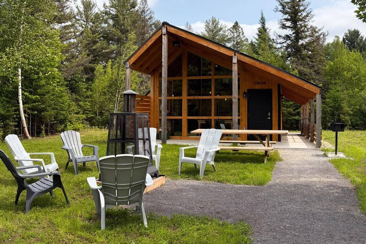 A wooden cabin with a large glass front, surrounded by outdoor seating and a gravel path.