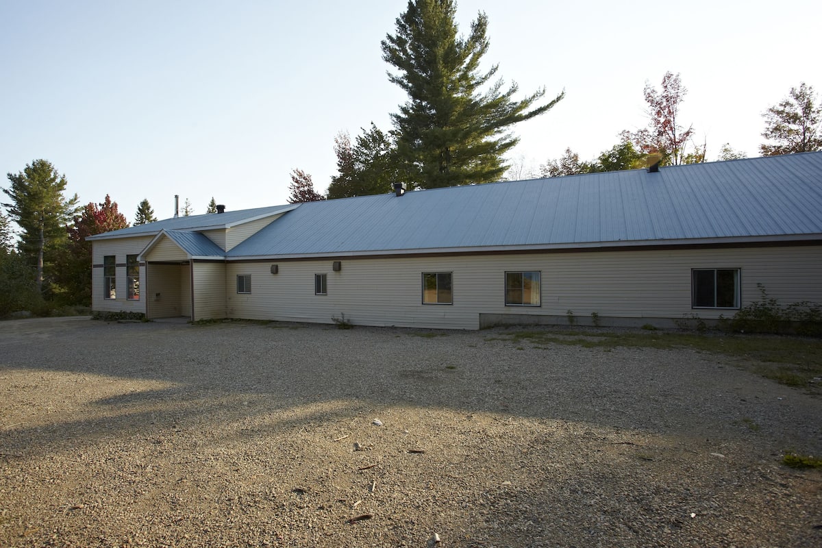 A single-story building with a metal roof, a gravel driveway, and a small porch area.