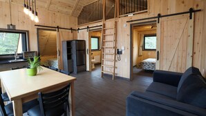 Un interior de madera con una mesa de comedor, sillas, un sofá, una zona de cocina y un altillo.