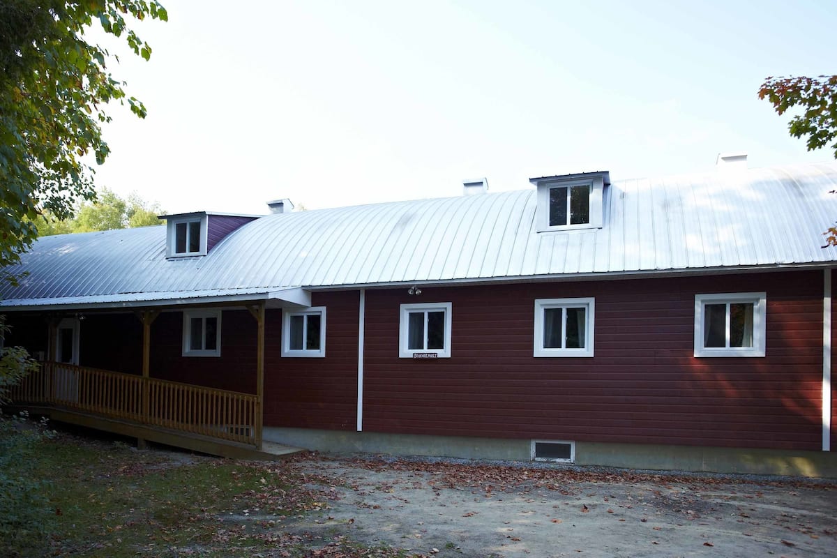 A two-story building with a metal roof, a wooden porch, and a small window on the upper floor.