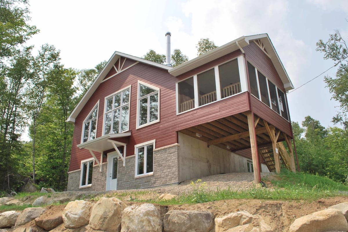 A two-story house with a stone foundation, large windows, and a wooden deck.