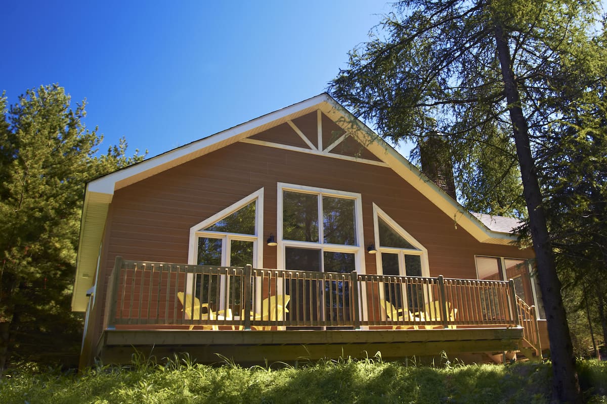A cabin with a wooden exterior, large windows, and a deck with chairs.