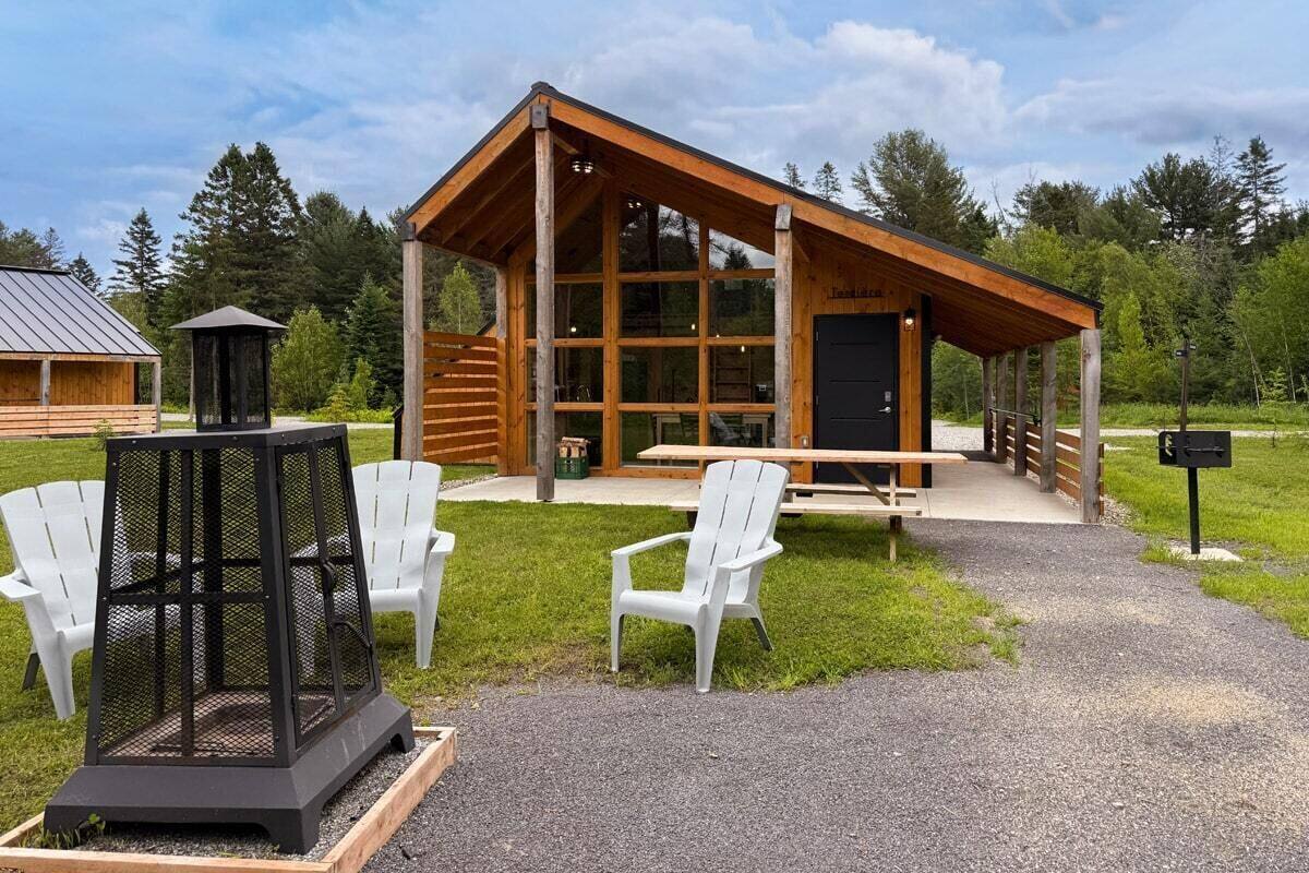 A cabin with a wooden exterior, large windows, and a covered picnic area.