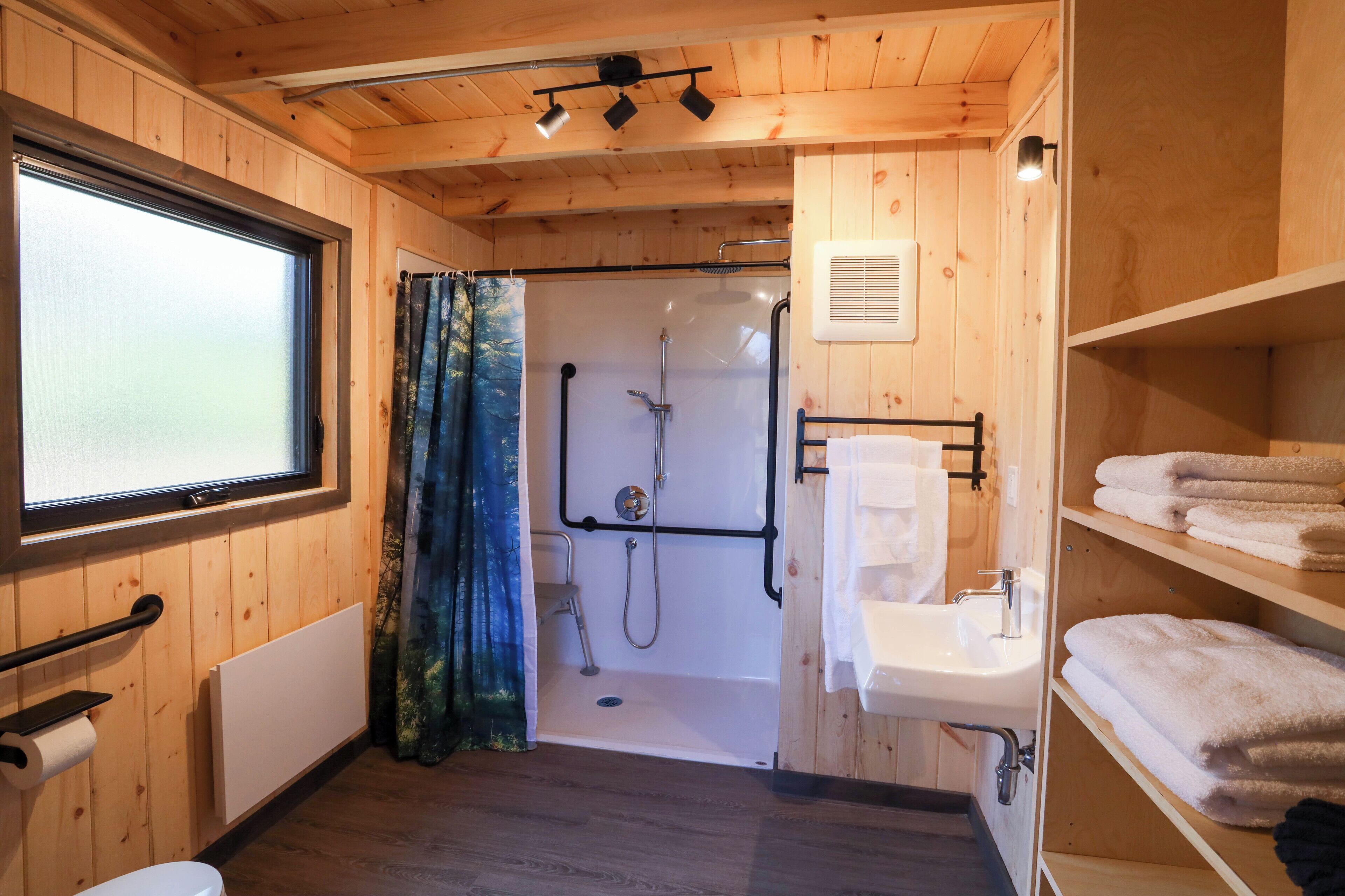 Een houten badkamer met een douche, wastafel en handdoekhouder.