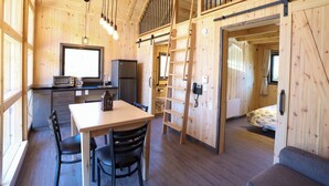Interior de una cabaña de madera con comedor, cocina y habitación en el altillo.