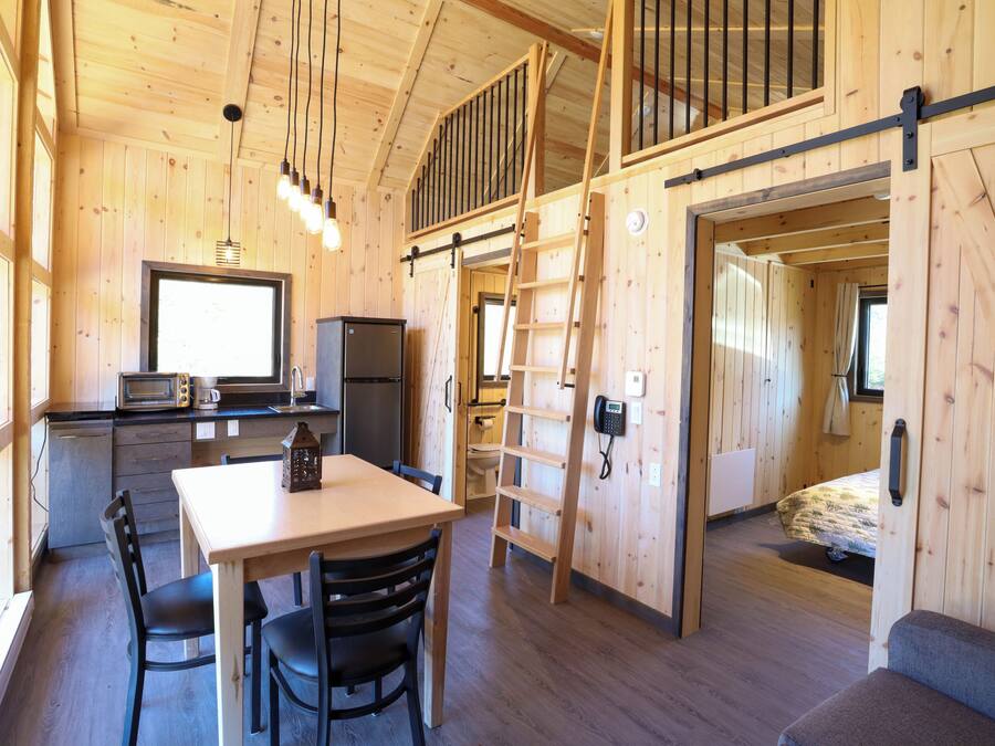 A wooden cabin interior with a dining area, kitchen, and a loft bedroom.