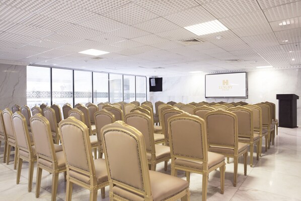 A conference room with rows of beige chairs, a projector screen, and a large window with a city view. - Luxury Hotel Inkari (Lima)