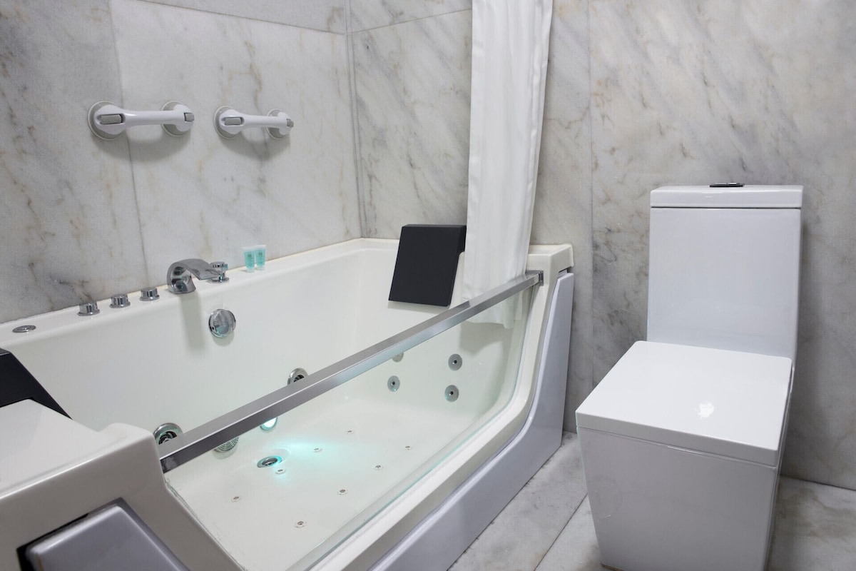 Un baño moderno con bañera de hidromasaje separada por vidrio, inodoro y zona de ducha.