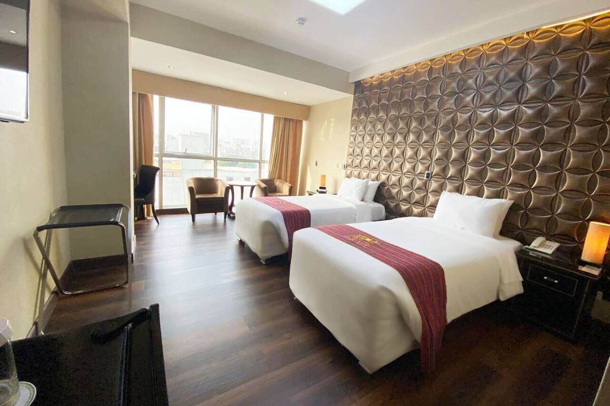 A hotel room with two beds, a sofa, a desk, and a large window.