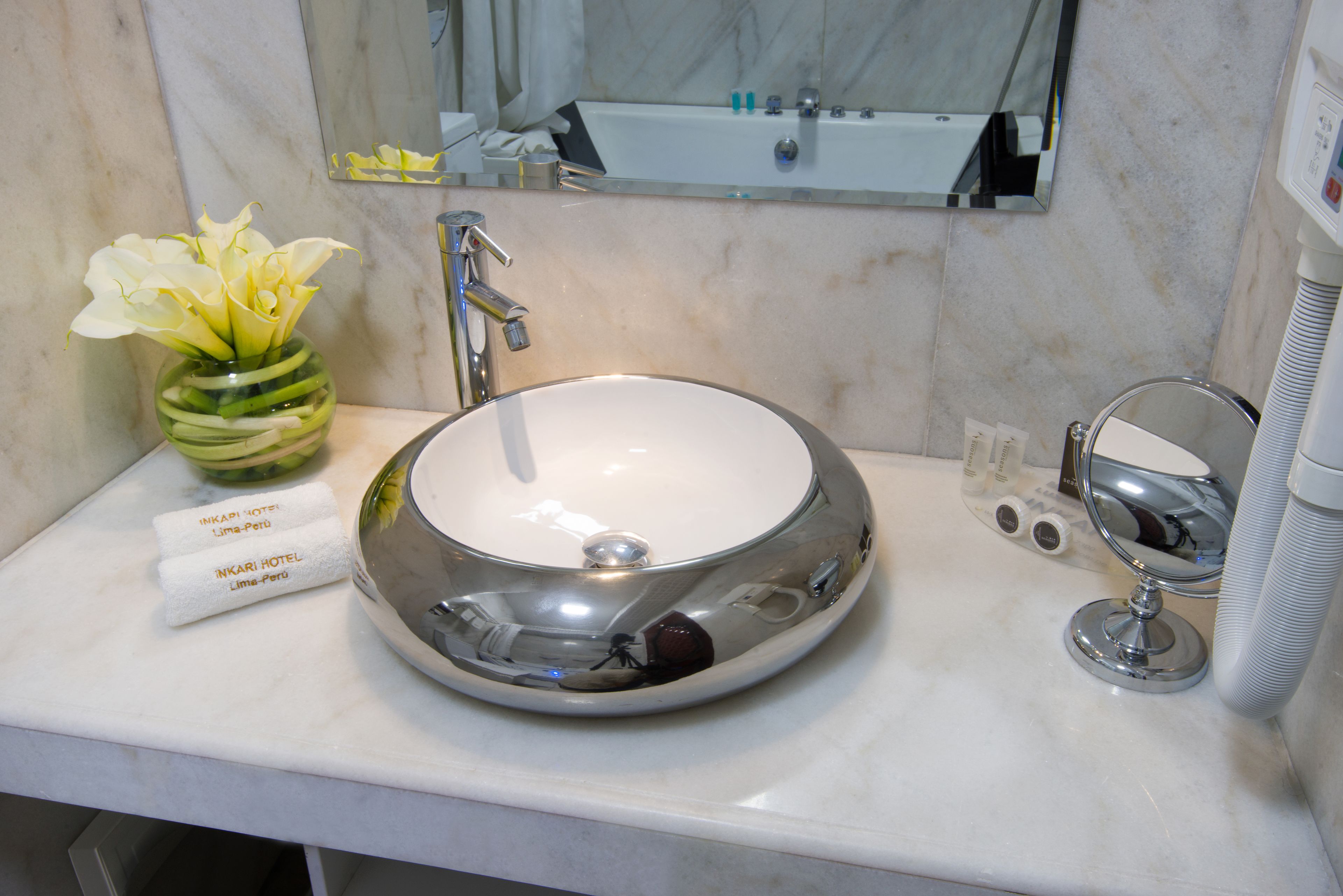 A bathroom with a round sink, a mirror, and a vase with flowers.