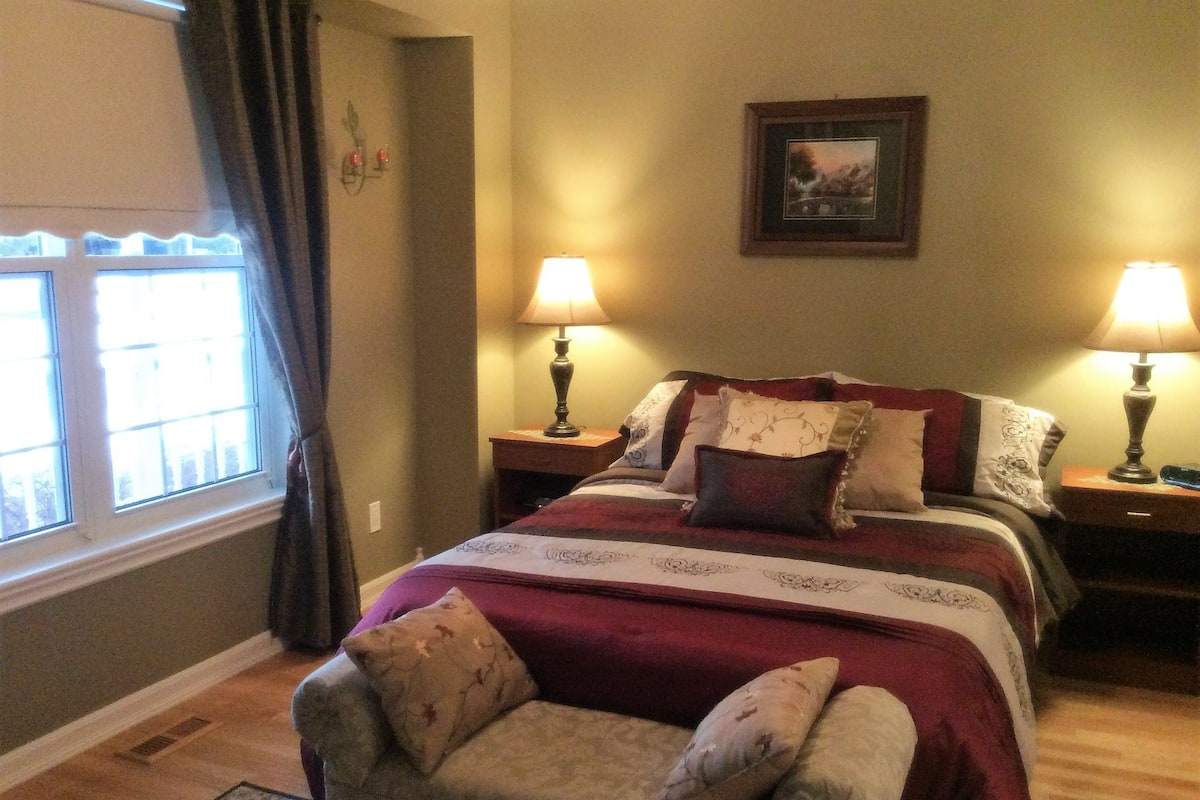 A neatly arranged bedroom with a large bed, two bedside tables with lamps, a chair, and a window with curtains.