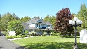 A two-story house with a porch, surrounded by a well-maintained lawn and trees. - The Boston 'T' B&B (Ottawa)