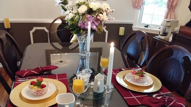 A dining table set for two with a vase of flowers, candles, and a glass of orange juice. - The Boston 'T' B&B (Ottawa)