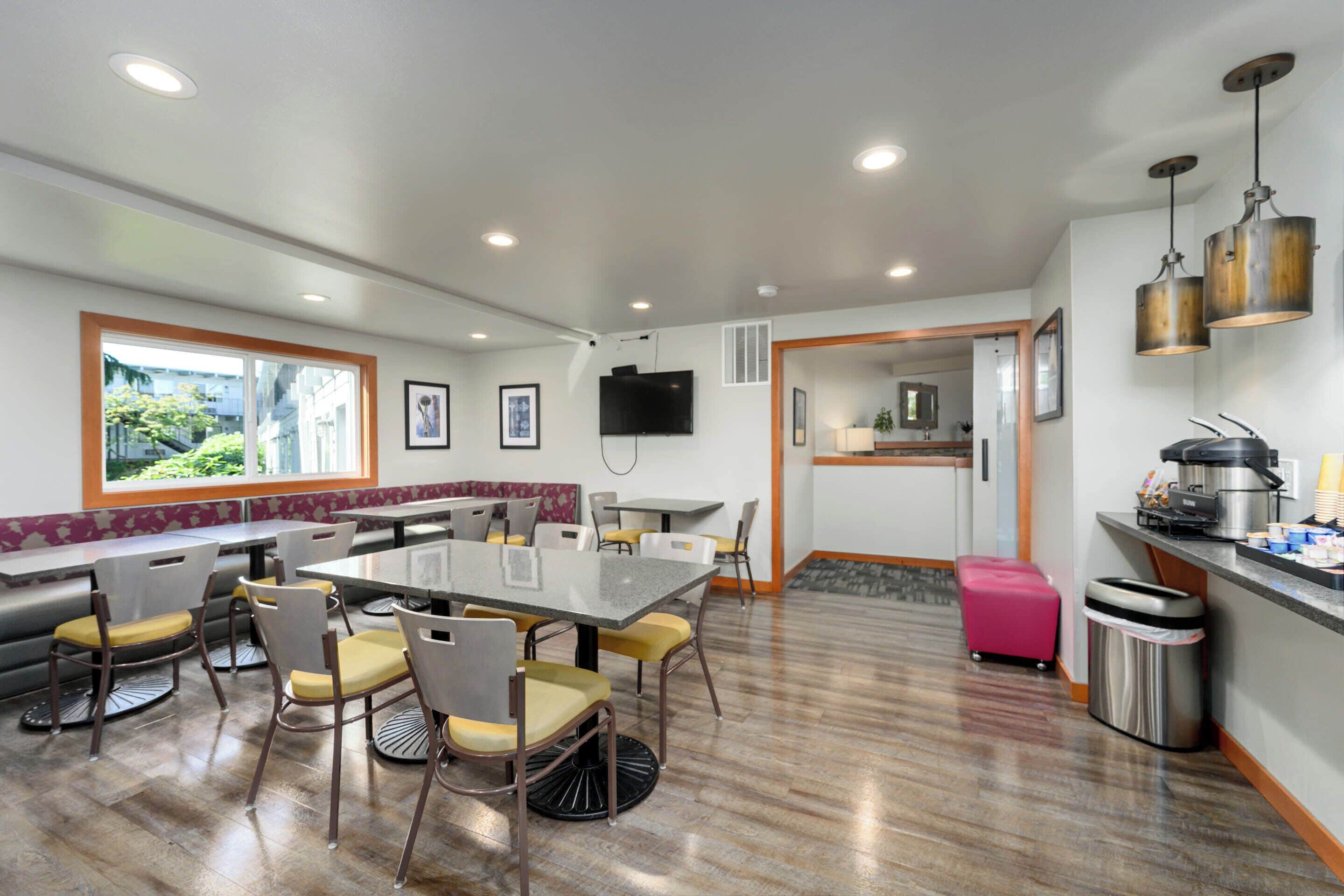 A modern dining area with a large table and chairs, a kitchen area with a sink and stove, and a window providing a view of the outdoors.