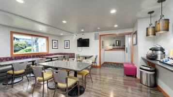A modern dining area with a large table and chairs, a kitchen area with a sink and stove, and a window providing a view of the outdoors.