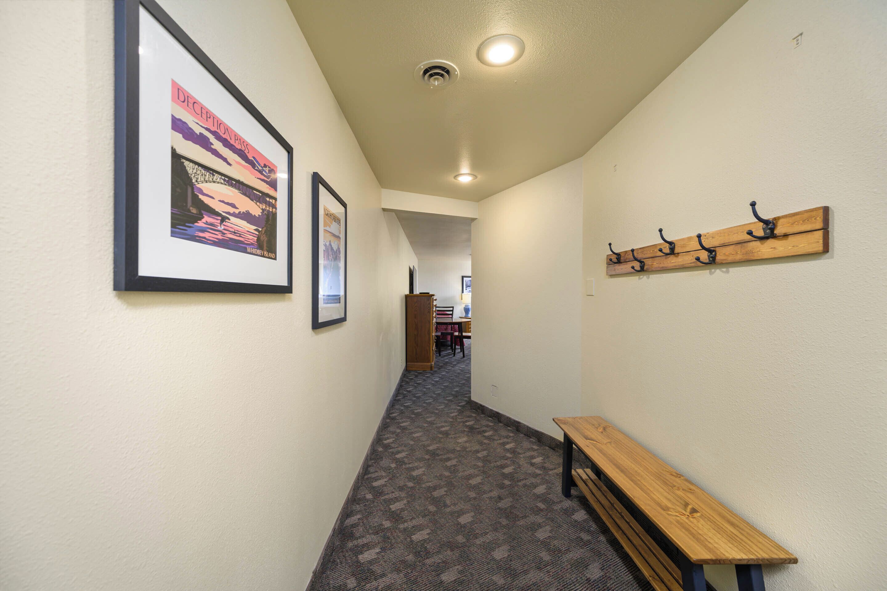 A hallway with a wooden bench, a coat rack, and framed pictures on the wall.