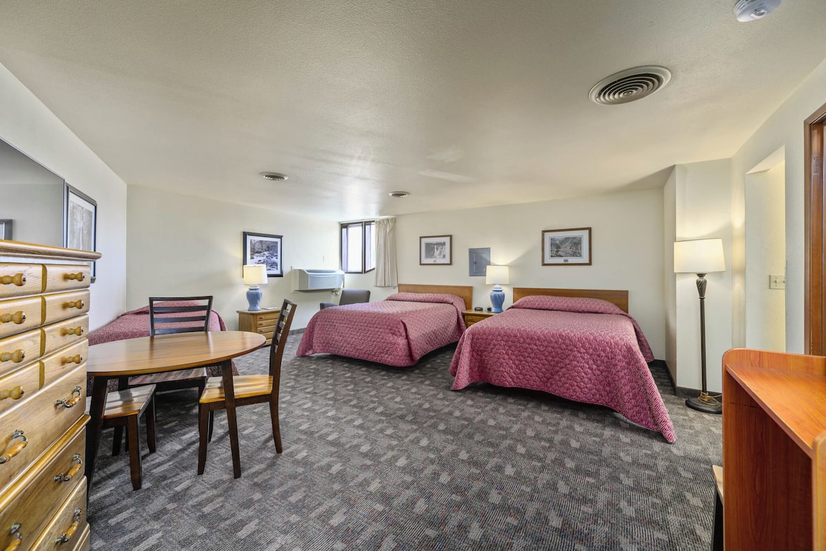 A hotel room with two beds, a dining table, chairs, a dresser, and a lamp.