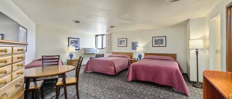 A hotel room with two beds, a dining table, chairs, a dresser, and a lamp.