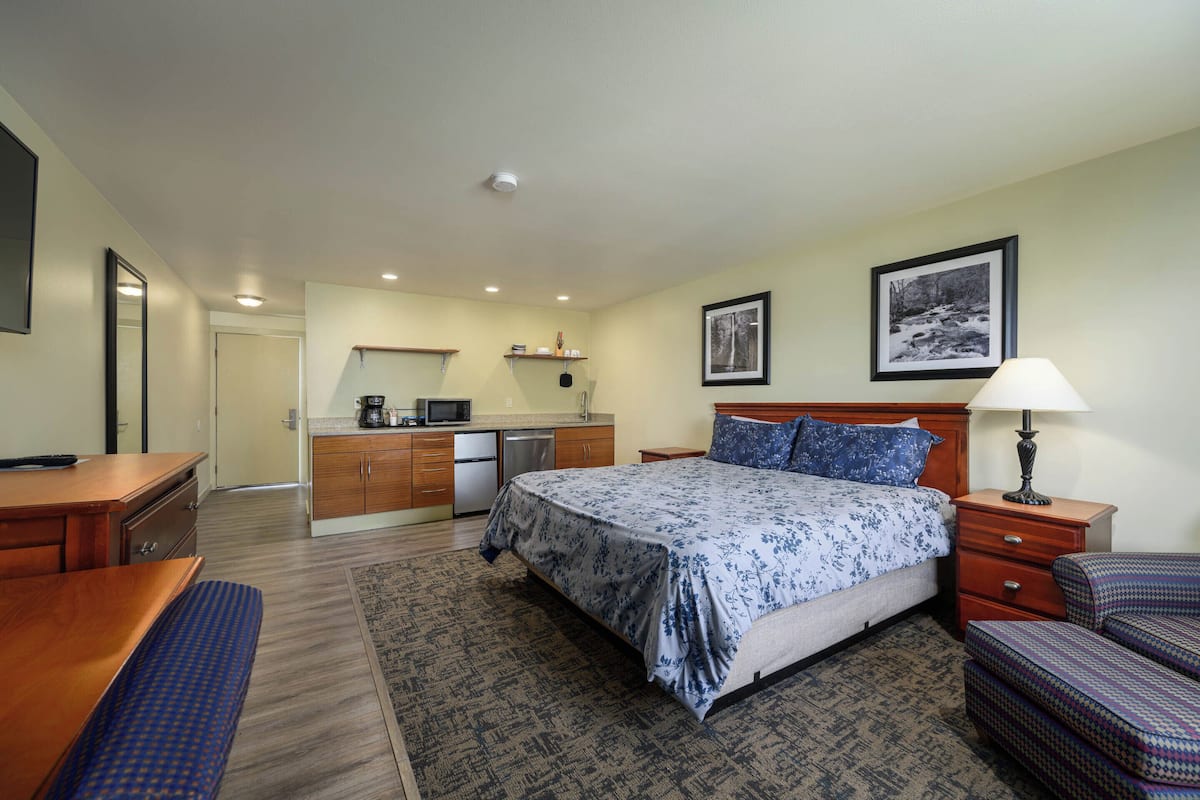 A hotel room with a bed, bedside table, lamp, and a small desk with a chair.