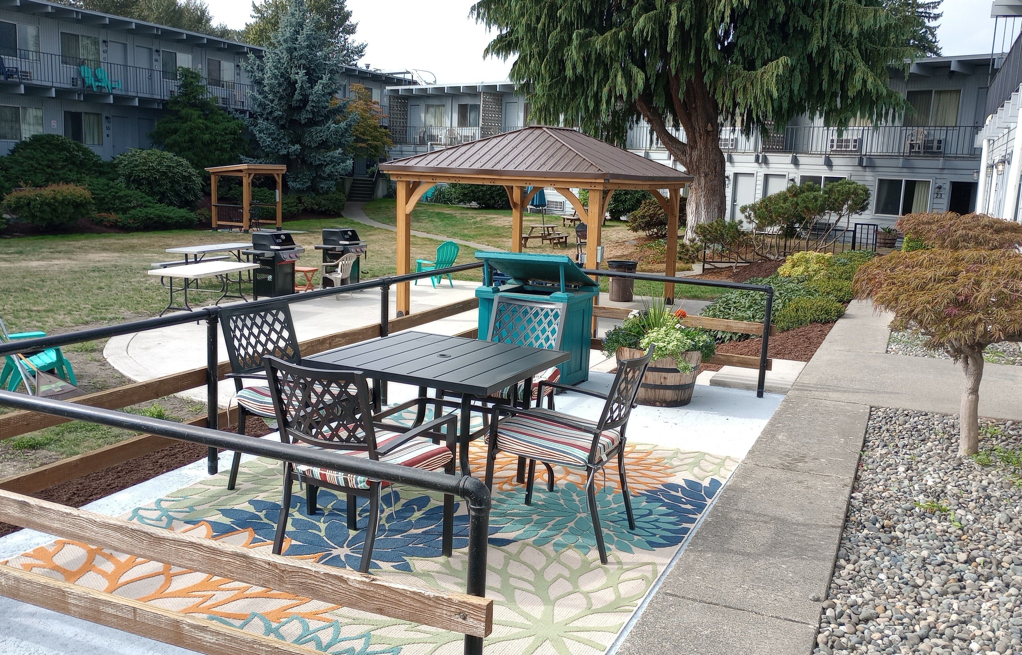Un patio al aire libre con un porche de madera, mesas, sillas y una zona de juegos infantil.