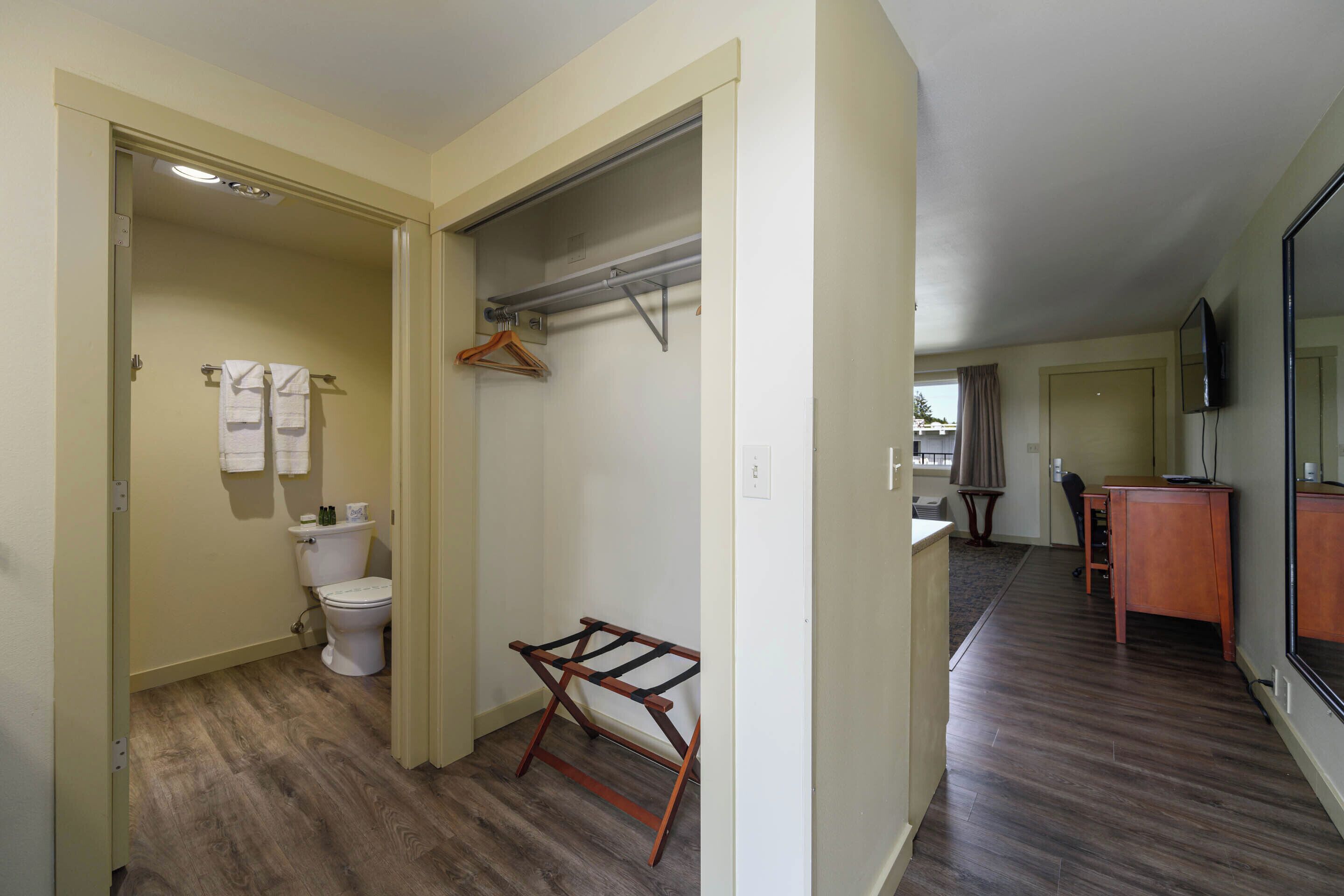 A hallway with a wooden floor, a hanging clothes rack, a toilet, and a mirror on the wall.