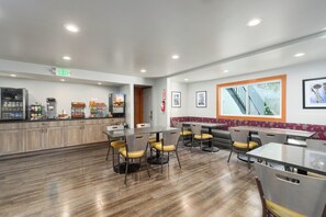 Un restaurante moderno con piso de madera, varias mesas y sillas de comedor, una zona de cocina con electrodomésticos y cuadros en las paredes.
