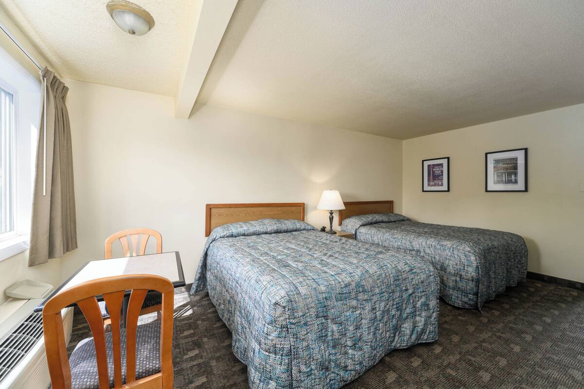 A hotel room with two beds, a desk, a chair, and a window with curtains.