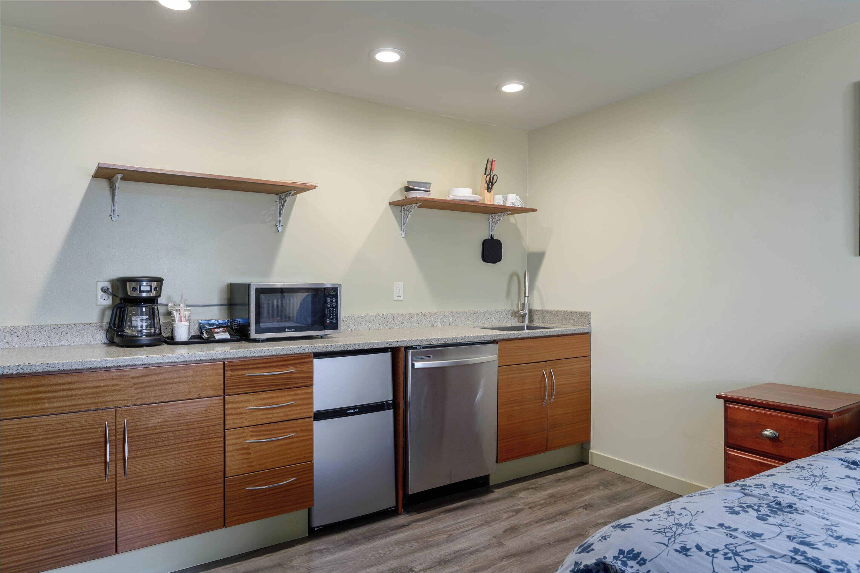 A compact kitchen with wooden cabinets, a stainless steel dishwasher, a microwave, and a coffee maker.