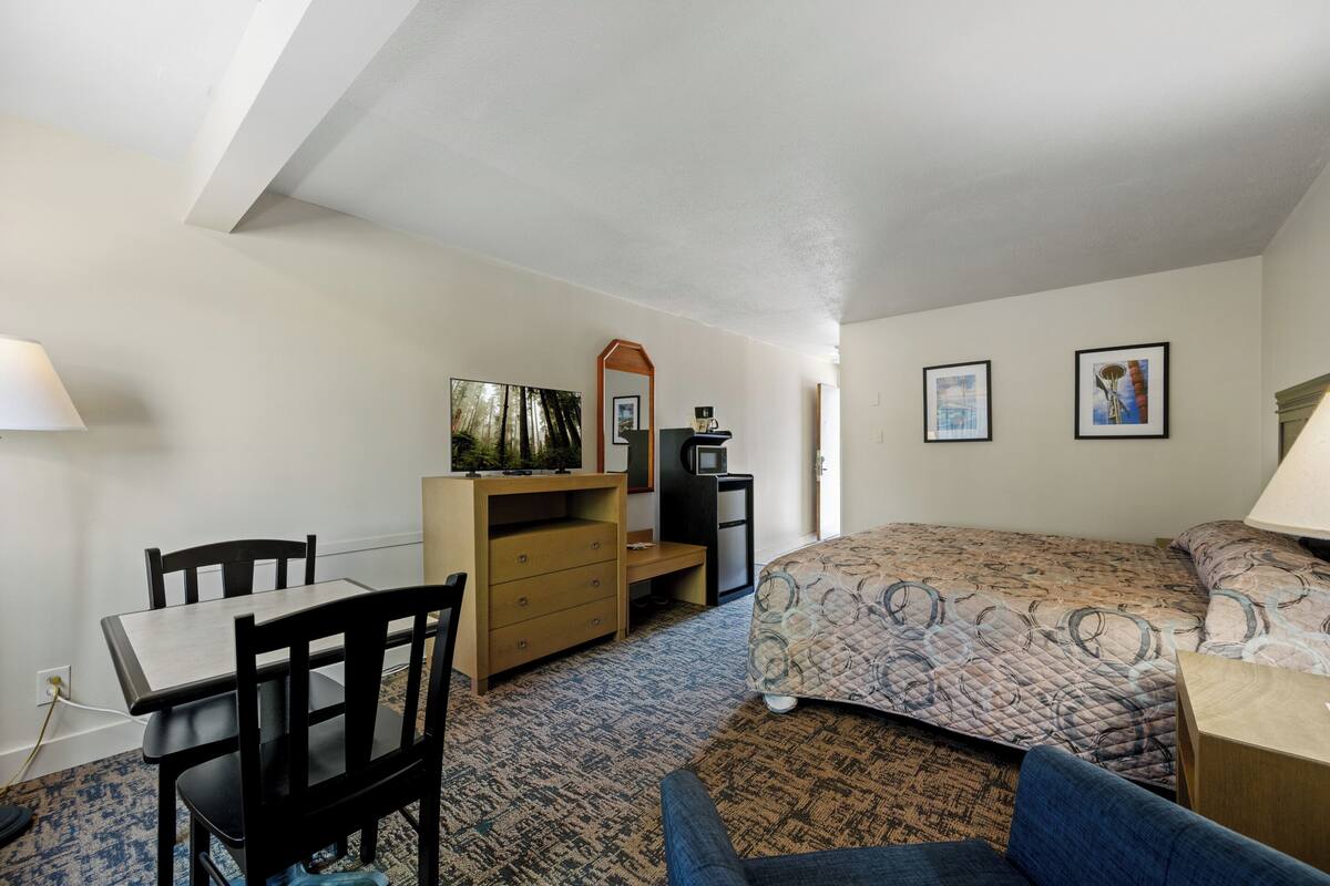 A bedroom with a bed, a desk, a chair, a dresser, a mirror, and two framed pictures on the wall.