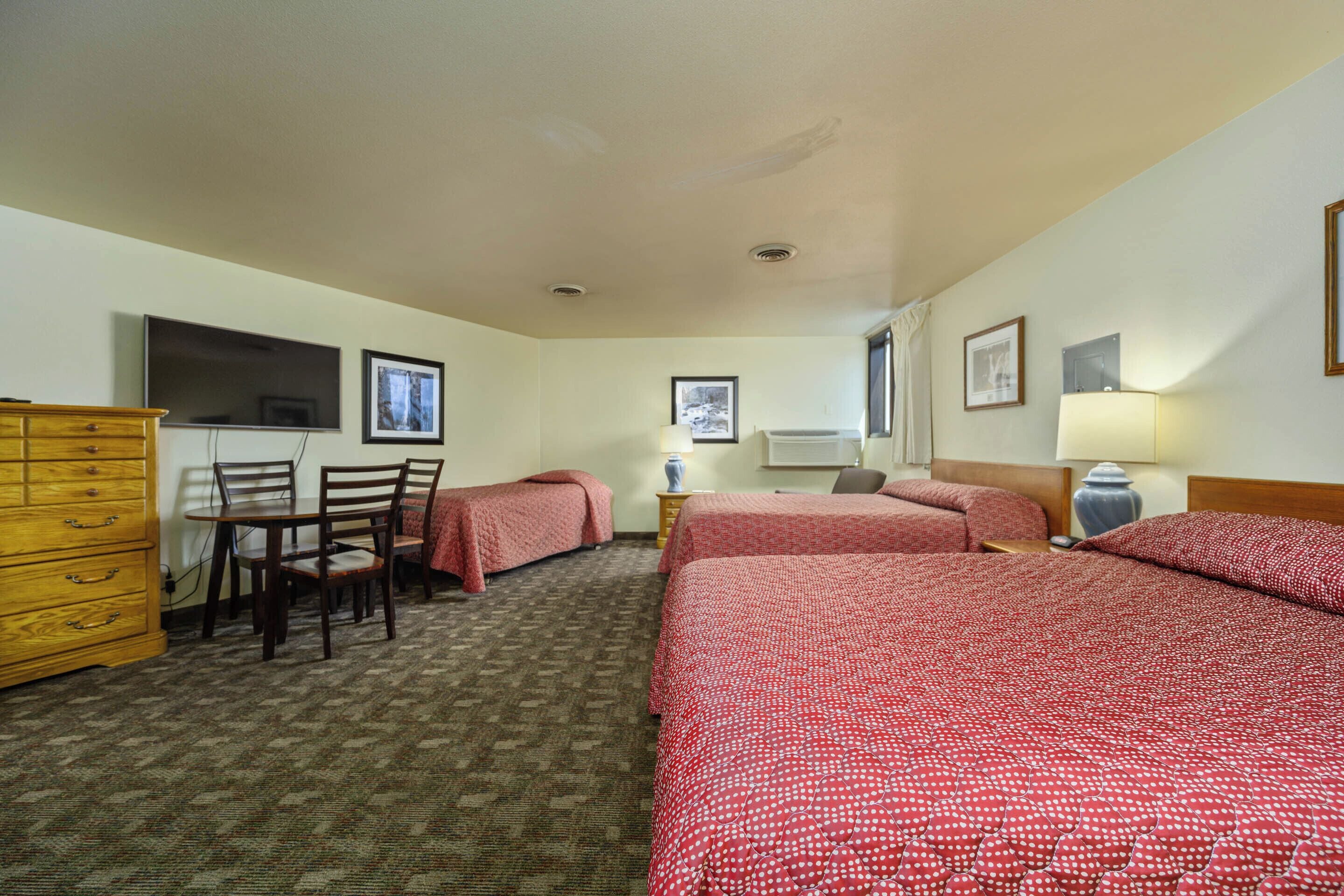 A hotel room with two beds, a wooden dresser, a desk with chairs, and a television.