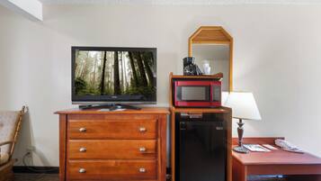 Ein Hotelzimmer mit einem Holzkapständer, einem Fernseher, der eine Waldszene zeigt, einer Mikrowelle, einer Lampe und einem Schreibtisch mit Telefon.