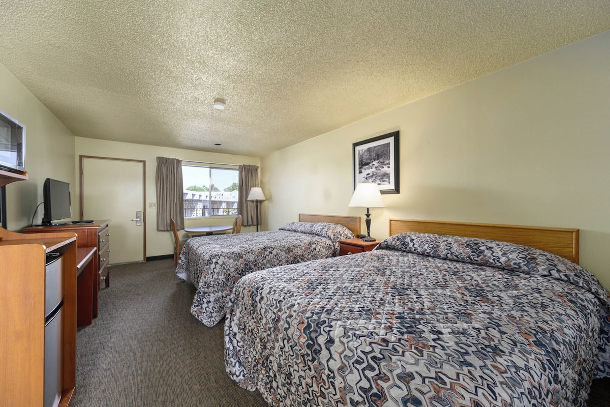 A hotel room with two beds, a desk with a television, a window with curtains, and a framed picture on the wall.