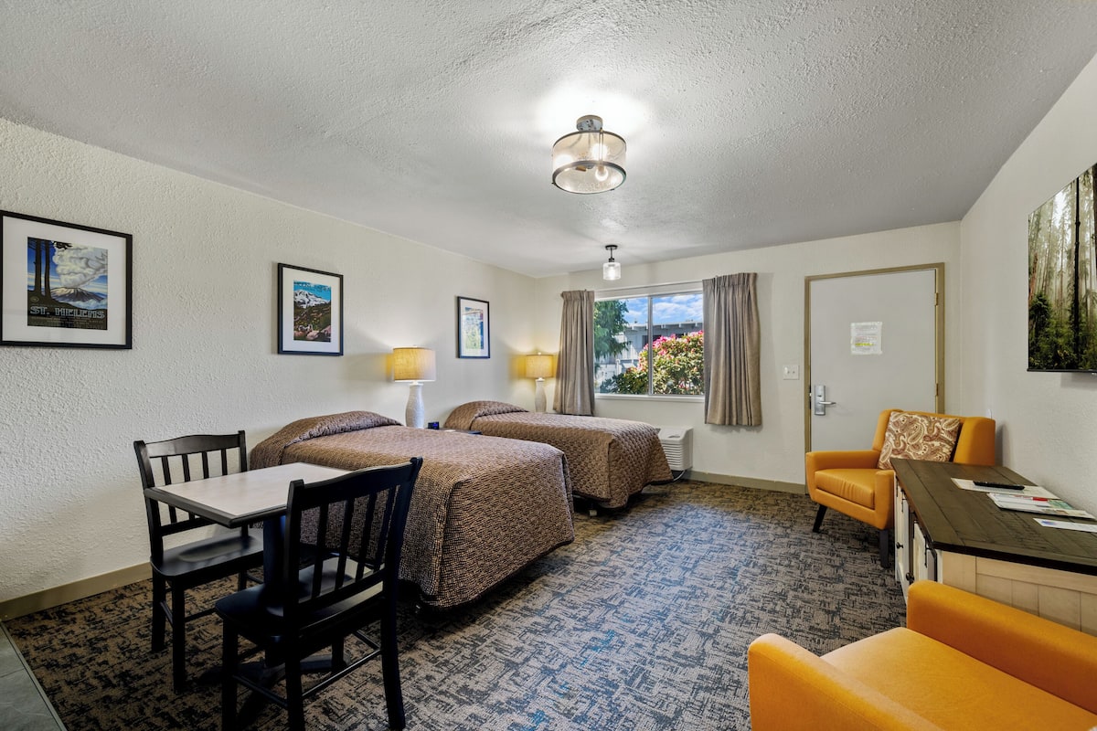 A hotel room with two beds, a desk, a chair, a table, and a window with curtains.