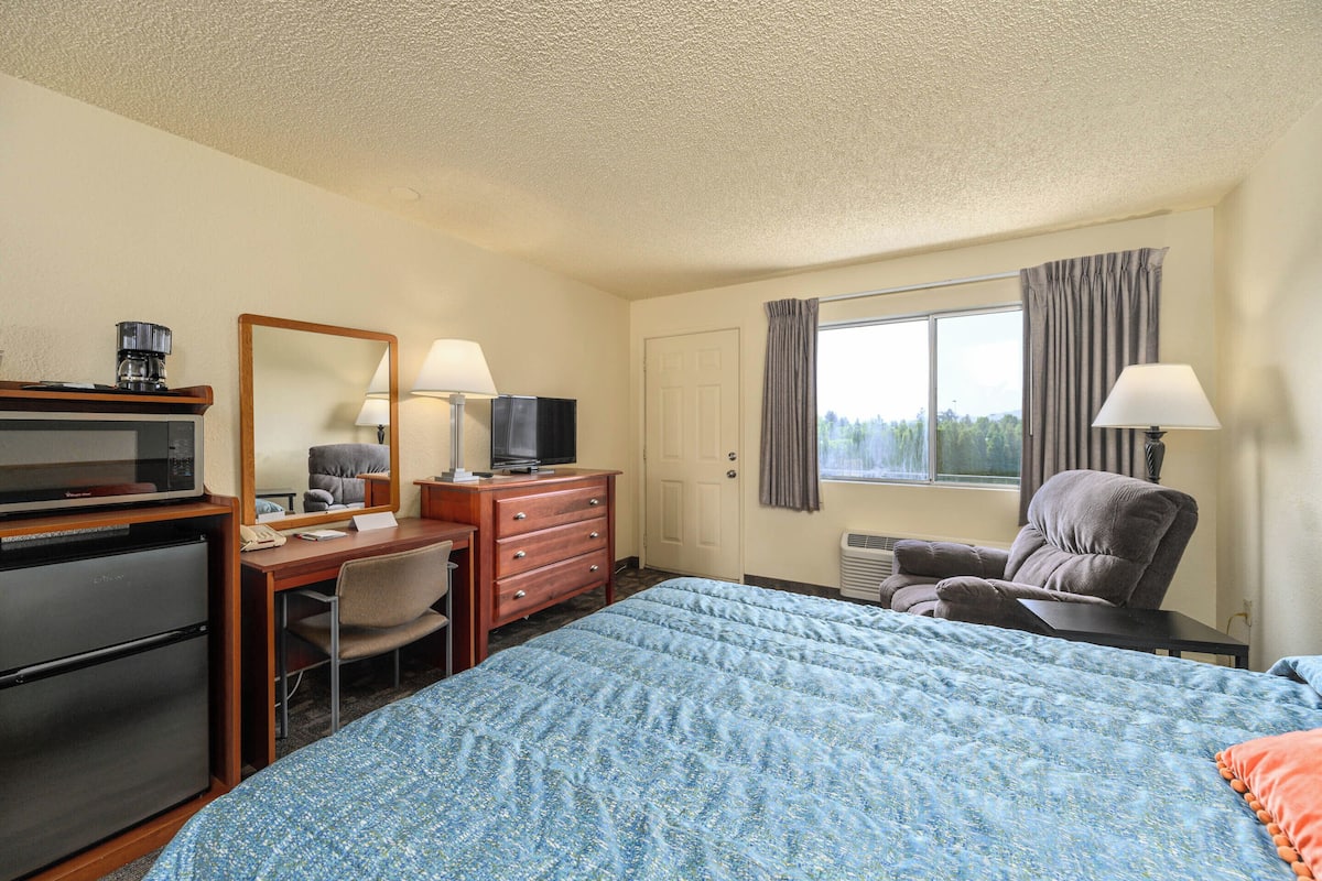 A hotel room with a bed, desk, chair, television, and a window with curtains.