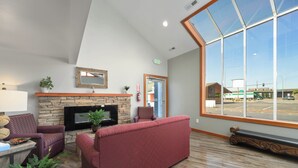 Un hall espacioso con chimenea de piedra, asientos cómodos, un ventanal con vistas al estacionamiento y un diseño moderno.