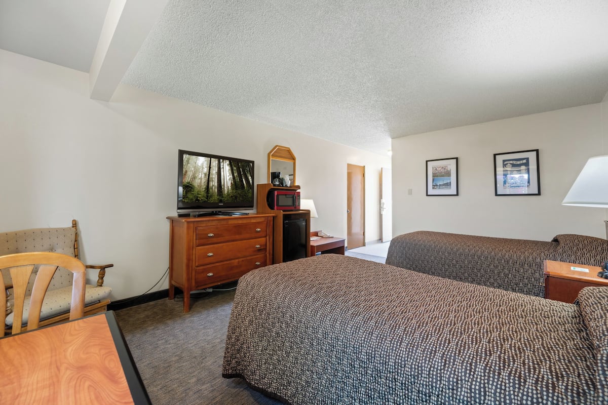 A hotel room with two beds, a desk, a chair, a dresser, a television, and framed pictures on the wall.