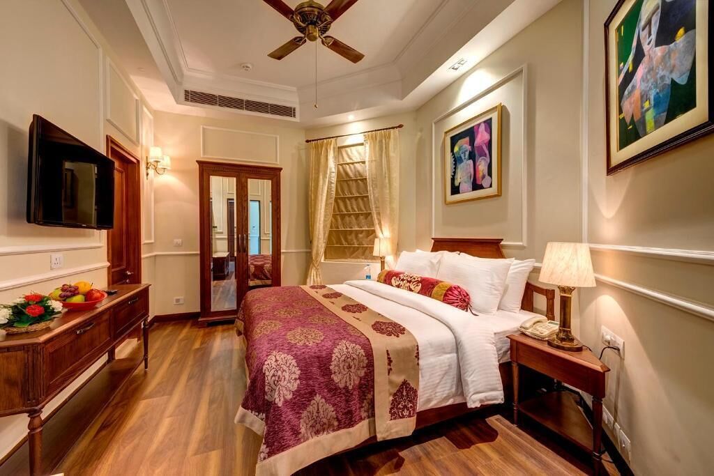 Una habitación de hotel con cama, mesita de noche, lámpara y una obra de arte en la pared.