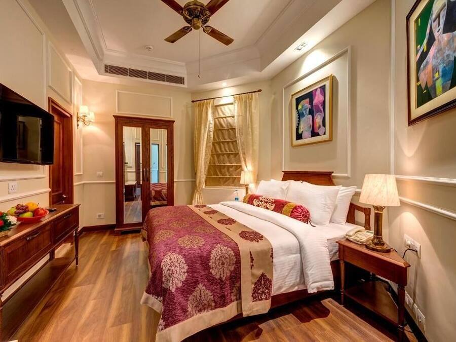 Una habitación de hotel con cama, mesita de noche, lámpara y una obra de arte en la pared.