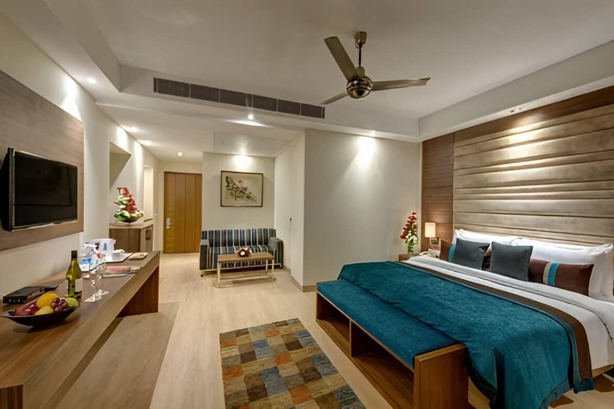Una habitación de hotel moderna con una cama, un escritorio con computadora, un televisor y un ventilador de techo.