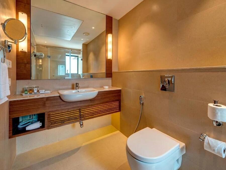 Uma casa de banho moderna com um espelho grande, uma pia, sanita e chuveiro.