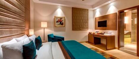Habitación de hotel con cama, escritorio, televisión y ventilador de techo.
